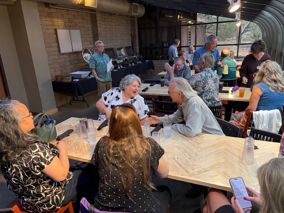 Members talking across dinner tables in a stone and timber dining room.